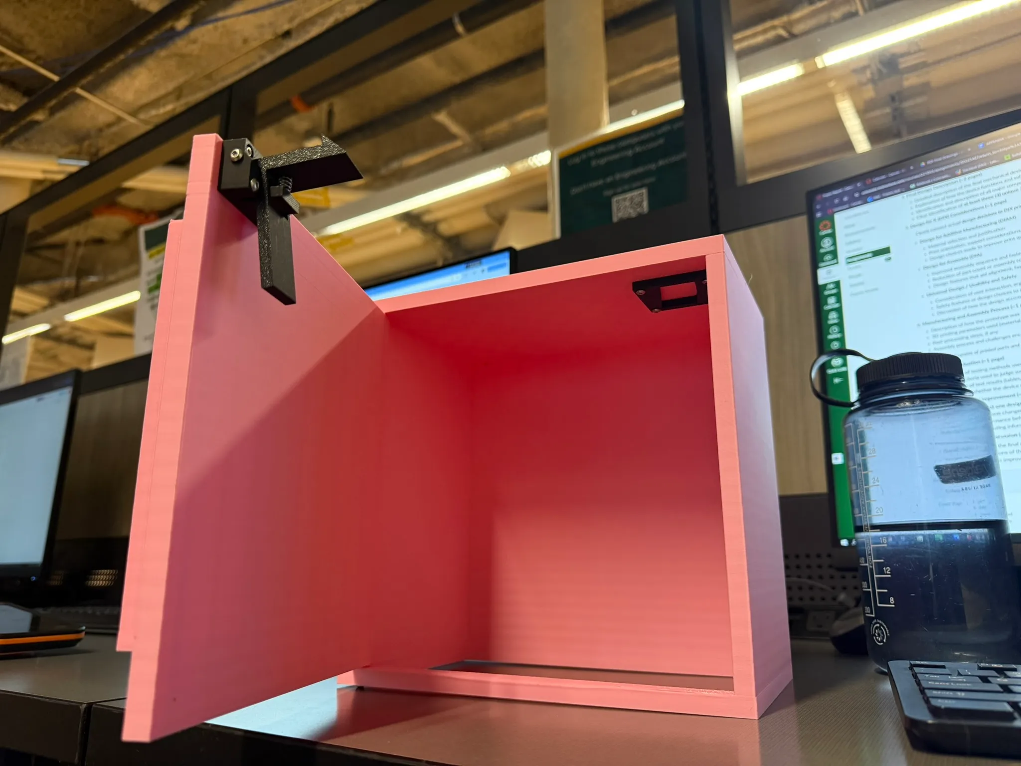 3D-printed test cabinet in pink PLA with the door open, showing the black latch mechanism