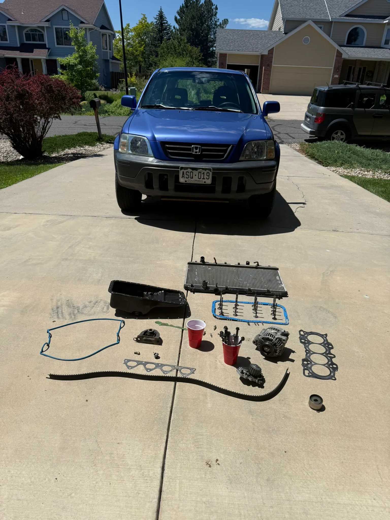Engine components laid out on the driveway during the rebuild — timing belt, gaskets, intake manifold, valve cover, and oil pan